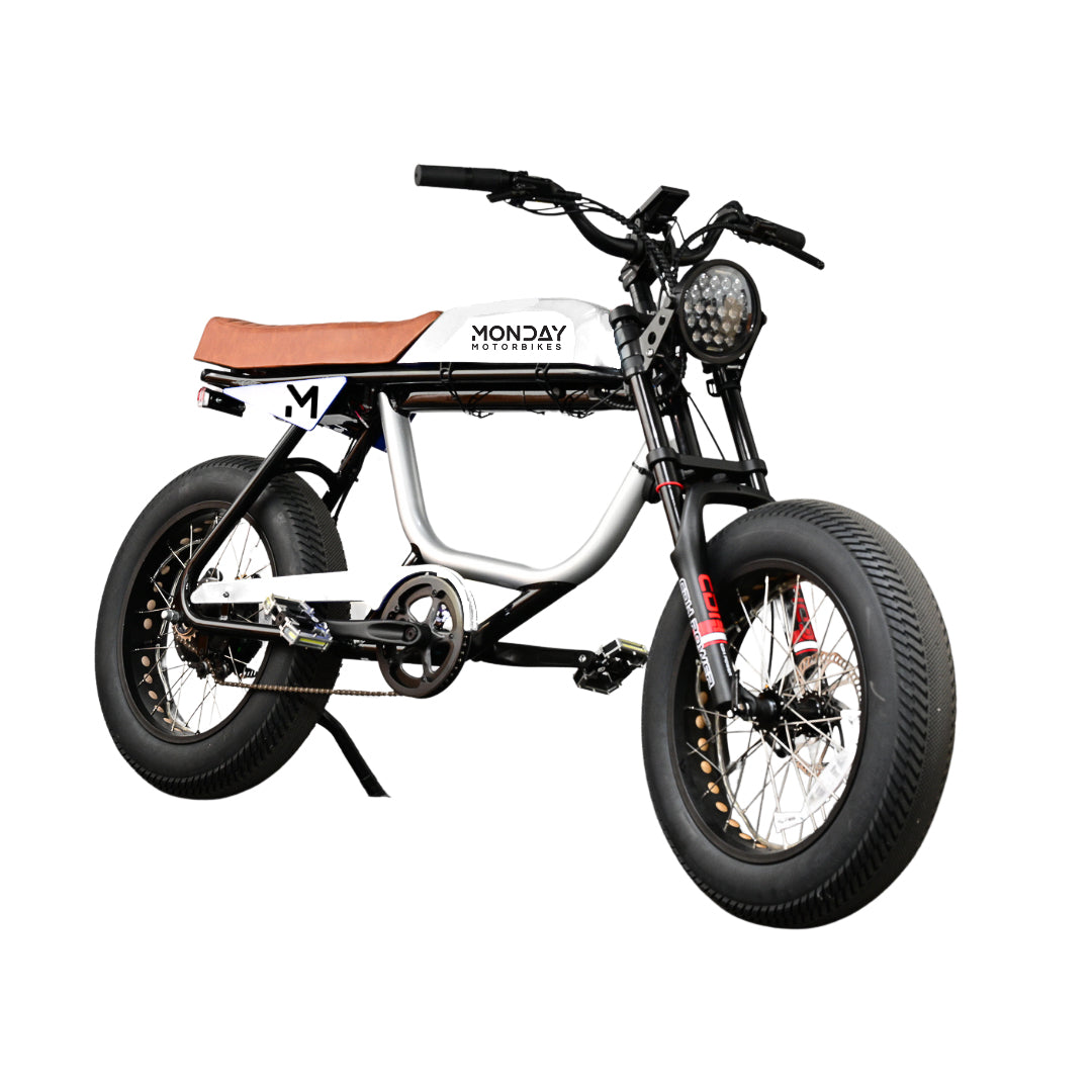 ANZA 1KW SR electric motorbike in white and black with cafe racer styling, featuring a tan leather seat, fat tires, high-rise handlebars, and distinctive honeycomb LED headlight. Side view showing the sleek aluminum frame and Monday Motorbikes branding.